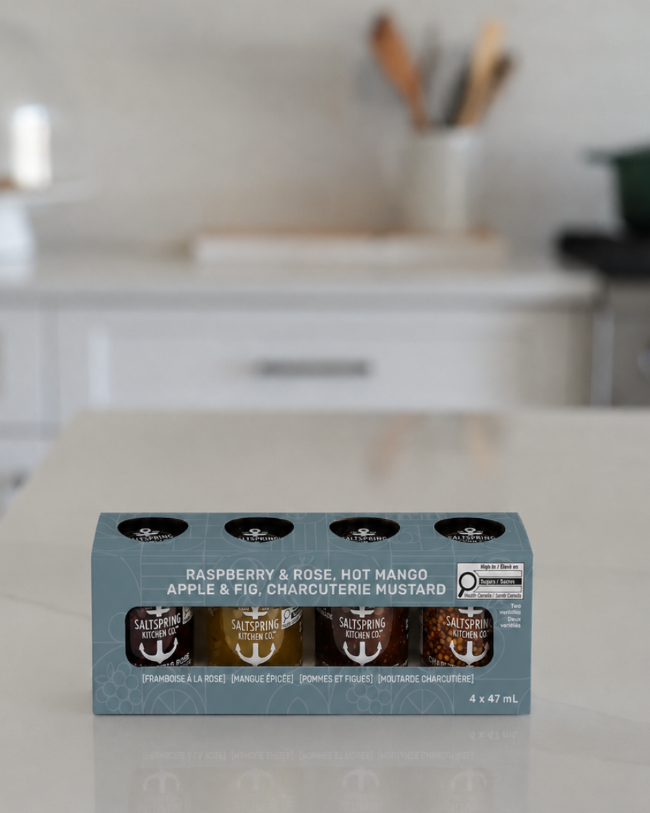 SaltSpring Kitchen Company Everyday Sampler Collection of four 47ml jars in a box set, sitting on a light countertop in a blurred kitchen setting. The packaging is a muted blue-gray with white text and graphics.