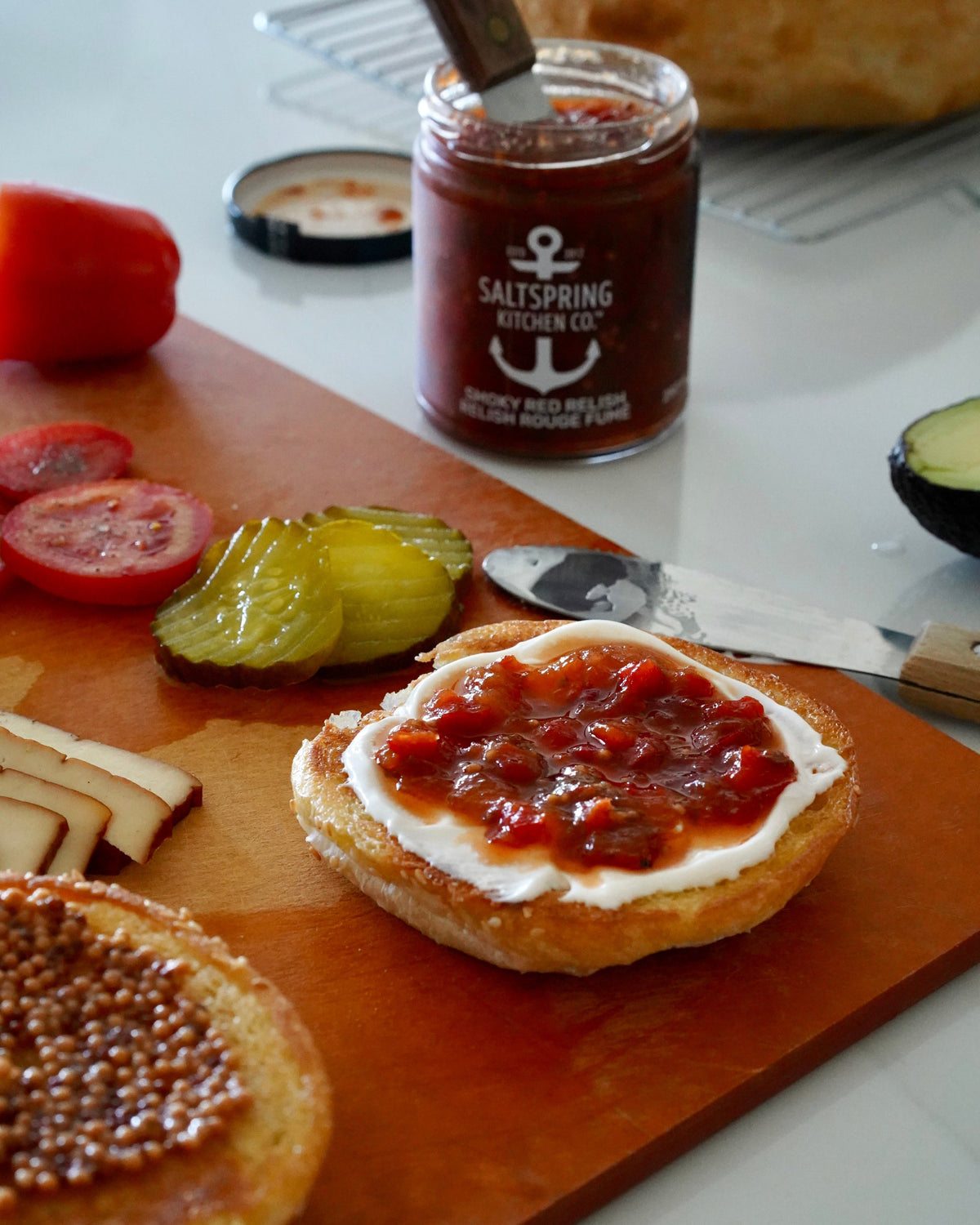 Open-faced sandwich with SaltSpring Kitchen Company Smoky Red Relish on may on a wooden cutting board with a jar of relish in the background.