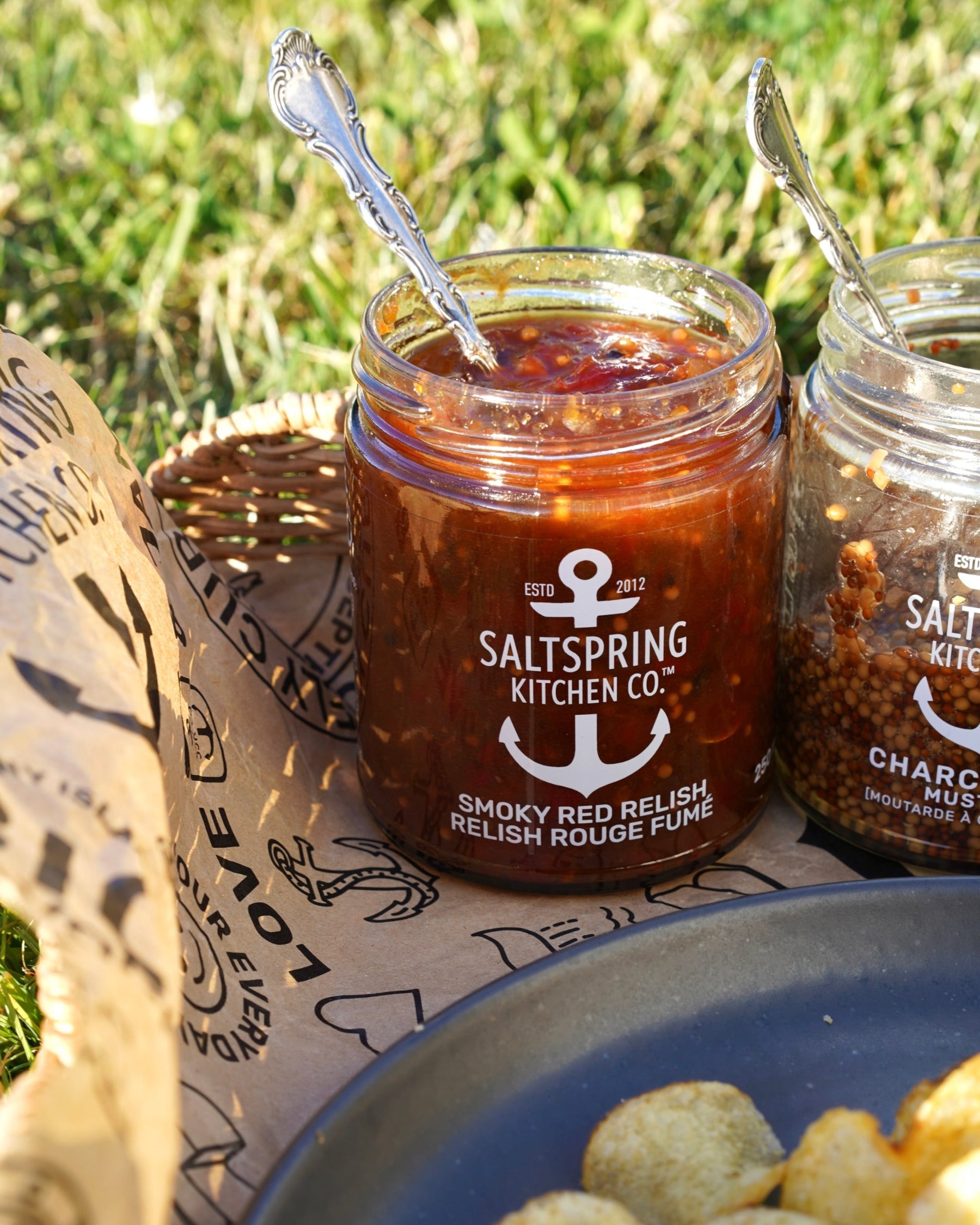 Jar of Saltspring Kitchen Co. Smoky Red Relish with a spoon in a tray outdoors.