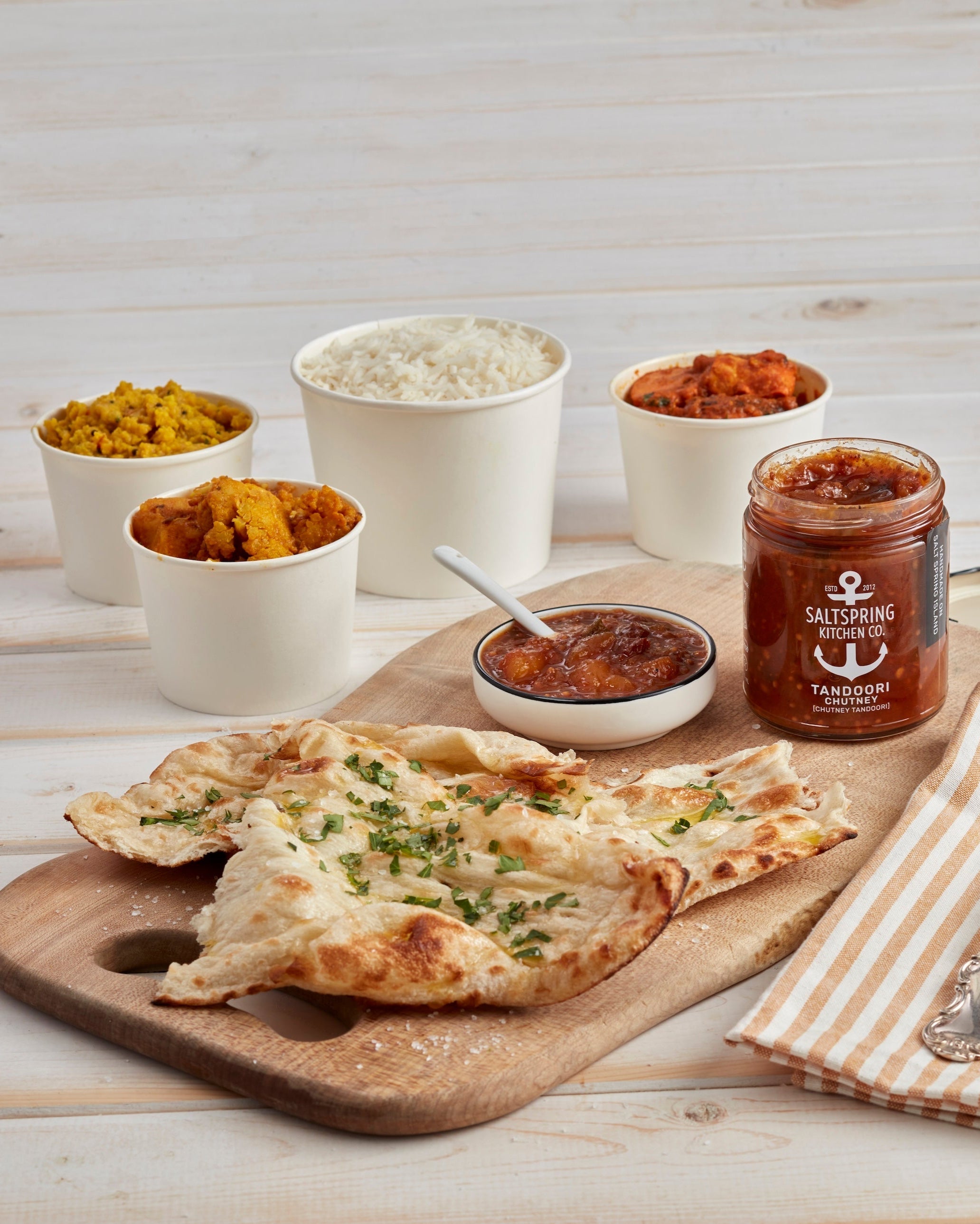 Plated meal with naan, tandoori chutney, and side dishes on a wooden board.