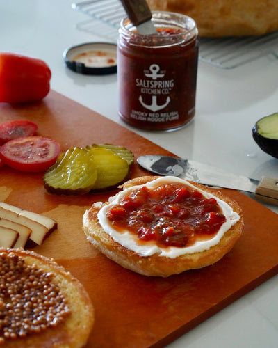 Open-faced sandwich with SaltSpring Kitchen Company Smoky Red Relish on may on a wooden cutting board with a jar of relish in the background.