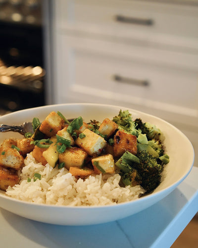 Bowl of food with rice, tofu, and broccoli on a kitchen counter.