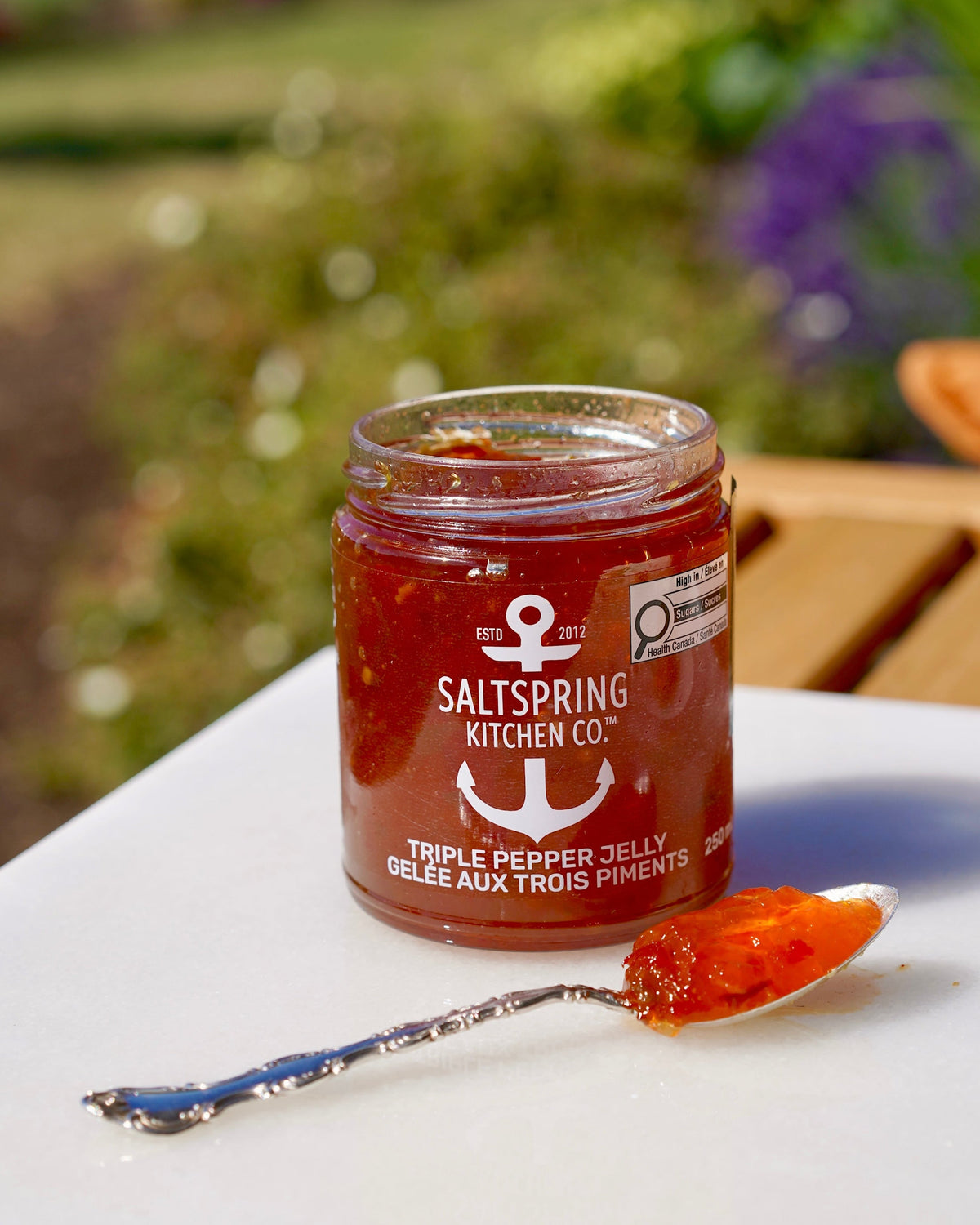 Jar of Saltspring Kitchen Co. triple pepper jelly on a white plate with a spoonful of jelly.