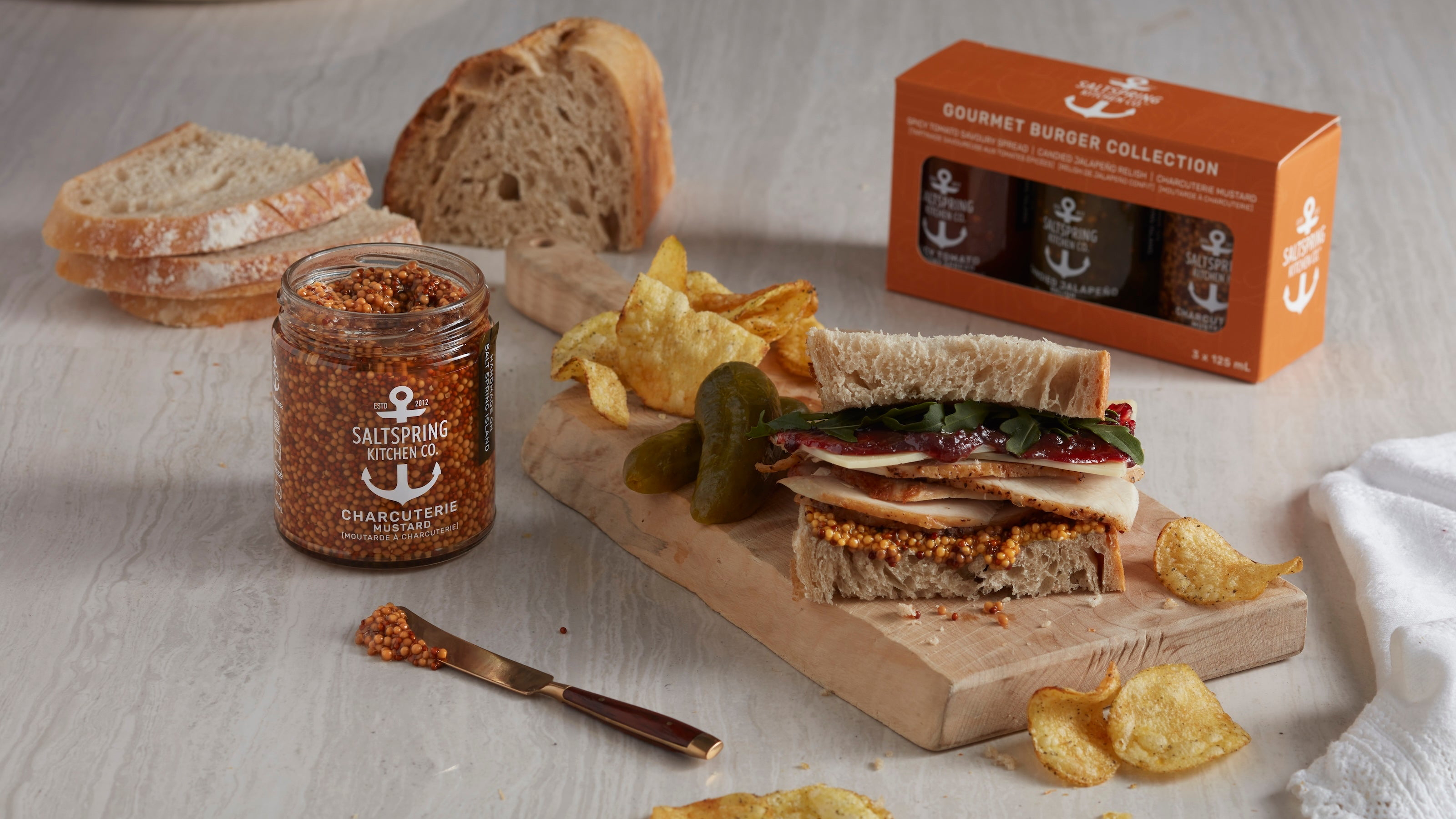 Gourmet burger collection with a sandwich, chips, and a jar of seasoning on a wooden board.