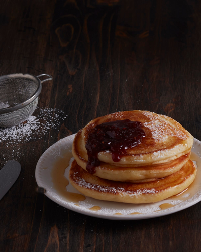 Stack of pancakes with syrup on a white plate with powdered sugar in the background